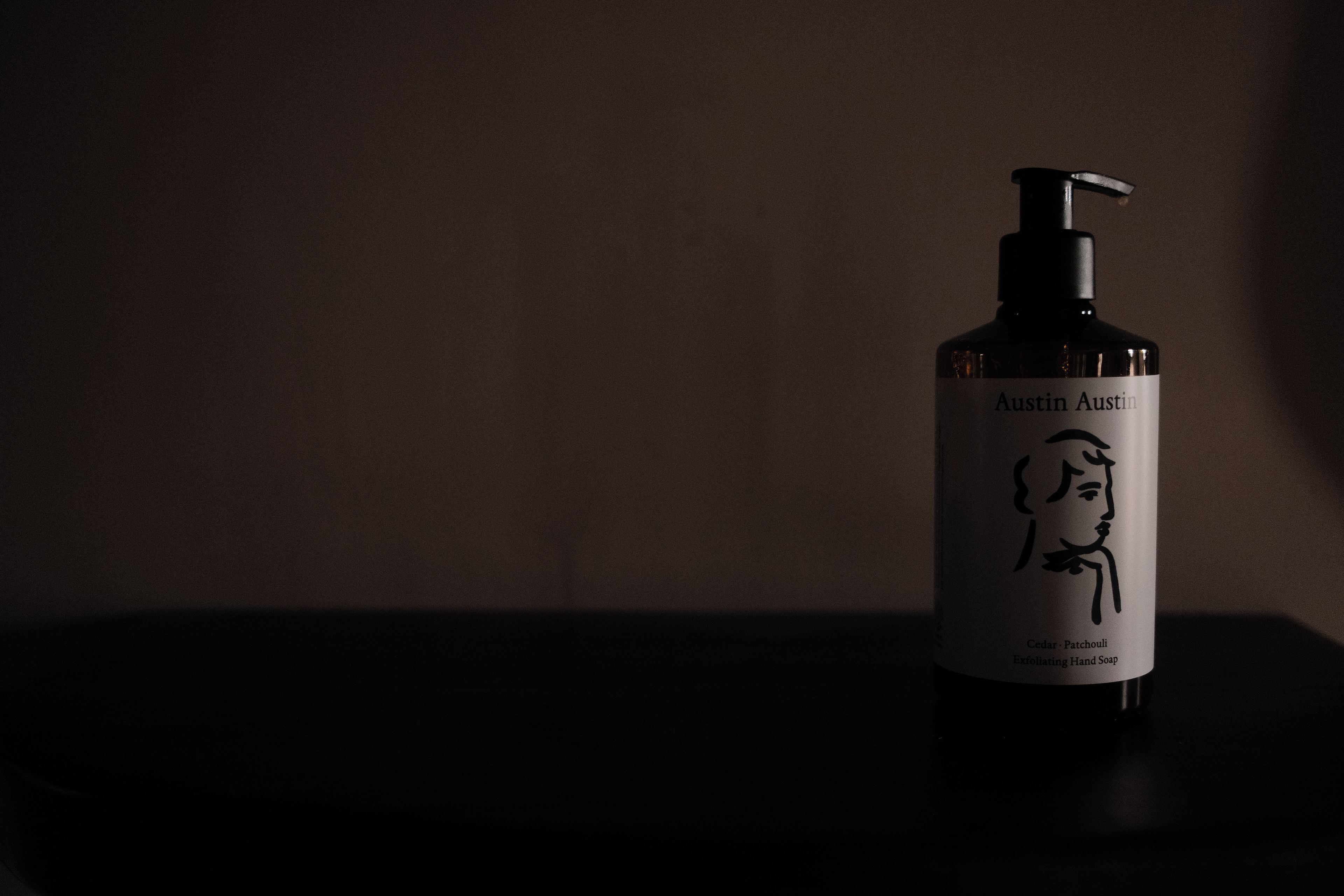 Una botella de Jabón Exfoliante para Manos Austin Austin sobre una superficie oscura.