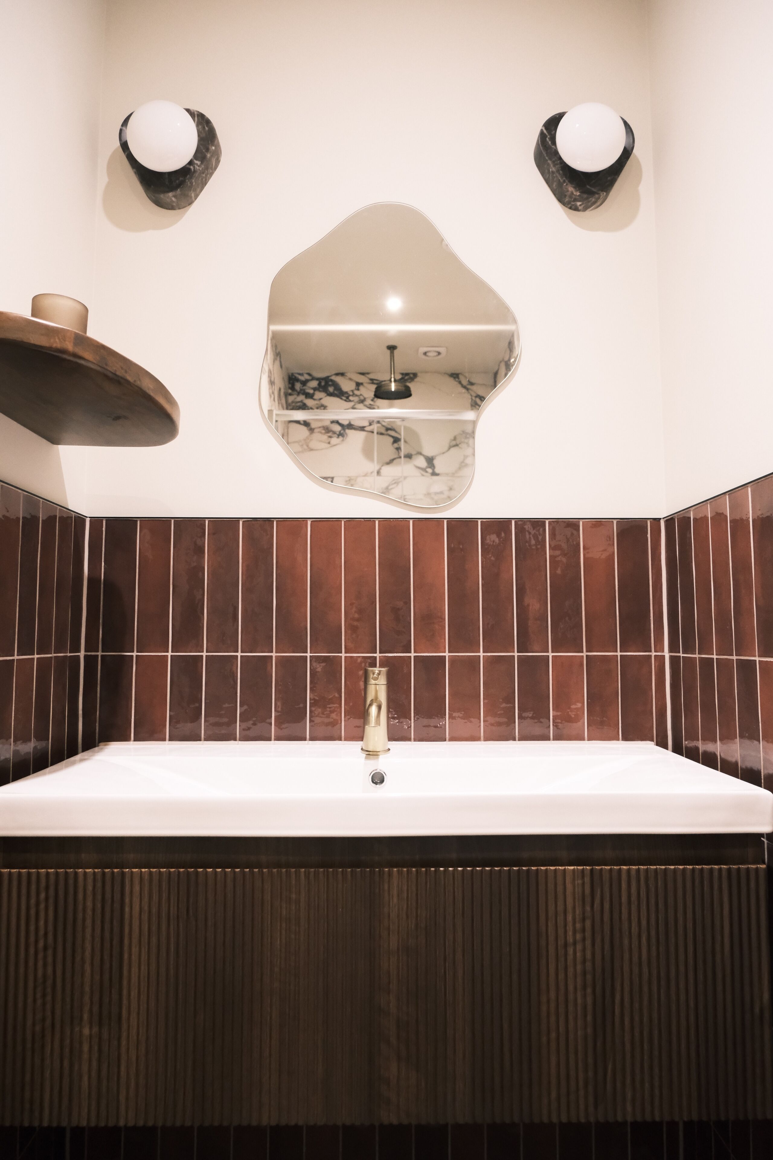 A bathroom with a large rectangular sink, dark brown tiled walls, and two wall-mounted lights.