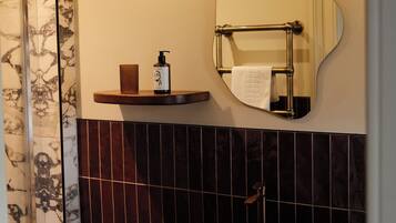 Une salle de bain avec un mur en marbre, un miroir rond, une étagère avec des articles de toilette et un lavabo noir.