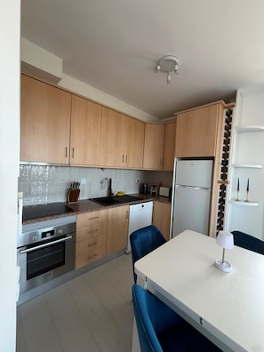 A modern kitchen with wooden cabinets, a built-in oven, a refrigerator, and a dining table with chairs. - Reformed Vintage Top Floor Stunning Views by Bento Box (Quarteira)
