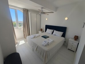 A hotel room with a large bed, a ceiling fan, a nightstand, and a view of the outdoors. - Reformed Vintage Top Floor Stunning Views by Bento Box (Quarteira)
