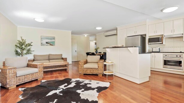 A modern living area with a sofa, a dining table, and a kitchen with white cabinets and appliances. - Victoria's Apartment | Riverfront, Pool, CBD (Rockhampton City)