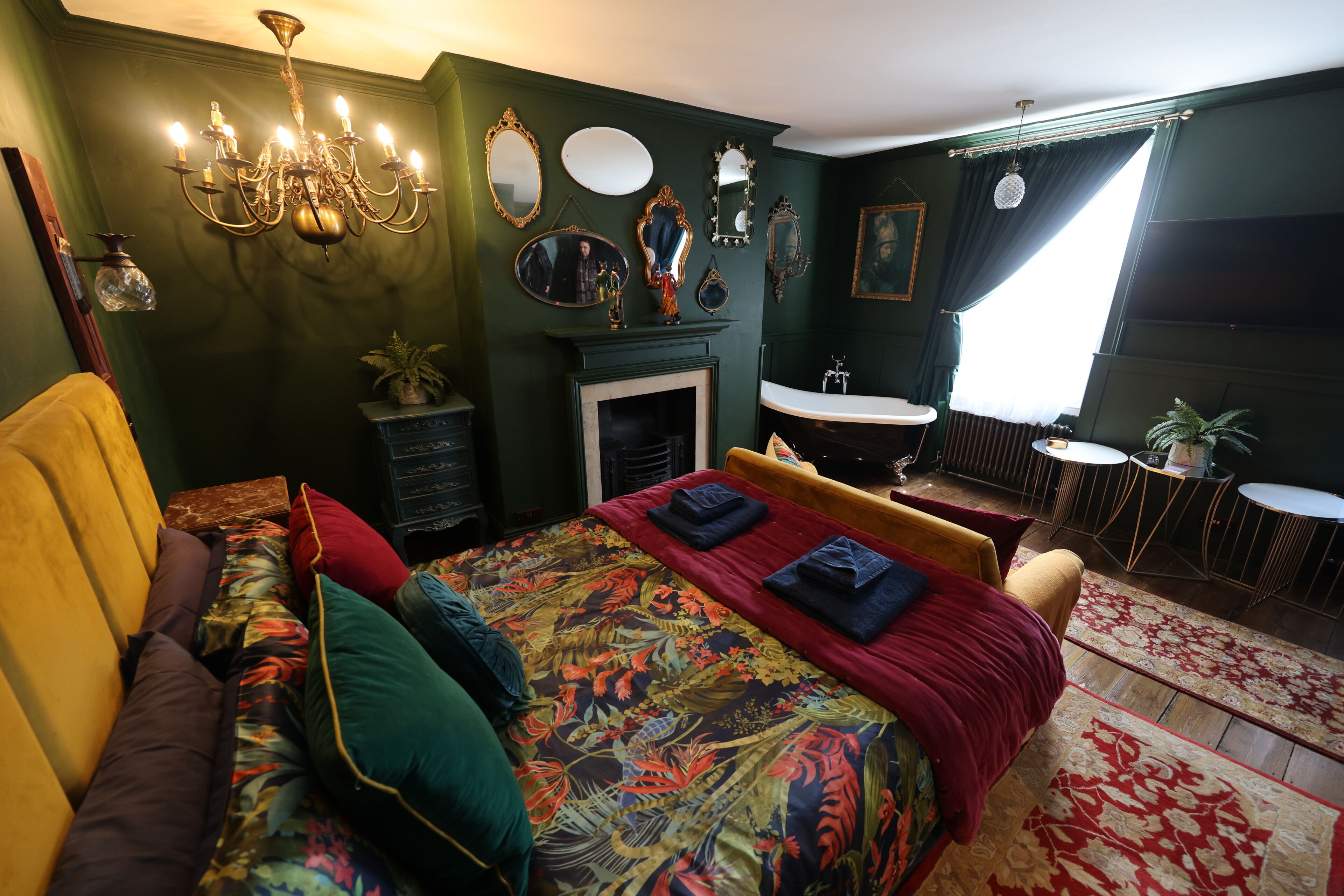 A room with a bed, a fireplace, a mirror, and a chandelier.