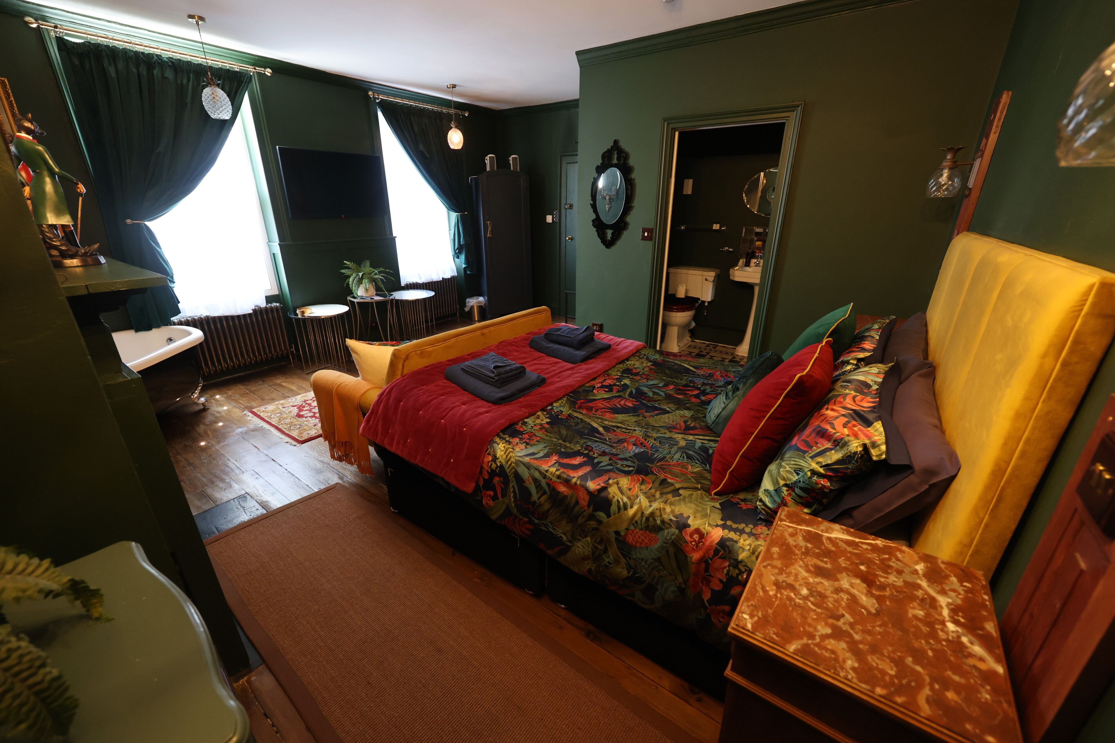 A bedroom with a bed, a bedside table, a mirror, and a window with curtains.