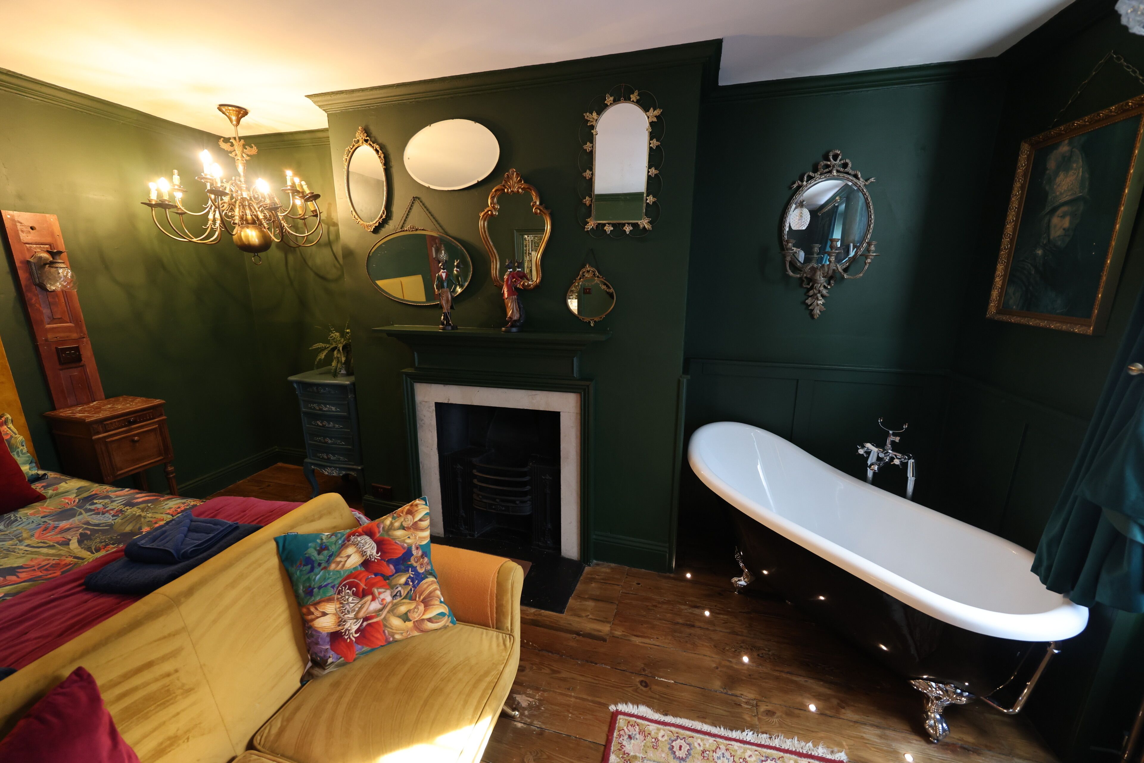A room with a bed, a sofa, a fireplace, a bathtub, and various wall-mounted mirrors and picture frames.