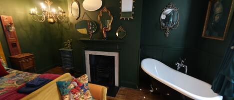 A room with a bed, a sofa, a fireplace, a bathtub, and various wall-mounted mirrors and picture frames.