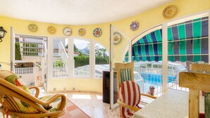 A room with wicker furniture, a pool view, and decorative plates on the wall. - Casa Nuestro Sueño for 4 People (Calpe / Calp)