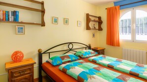 A bedroom with a bed, a nightstand, a dresser, a window with curtains, and shelves with books and pictures. - Casa Nuestro Sueño for 4 People (Calpe / Calp)