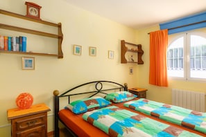 Ein Schlafzimmer mit einem Bett, einem Nachttisch, einer Kommode, einem Fenster mit Vorhängen und Regalen mit Büchern und Bildern.