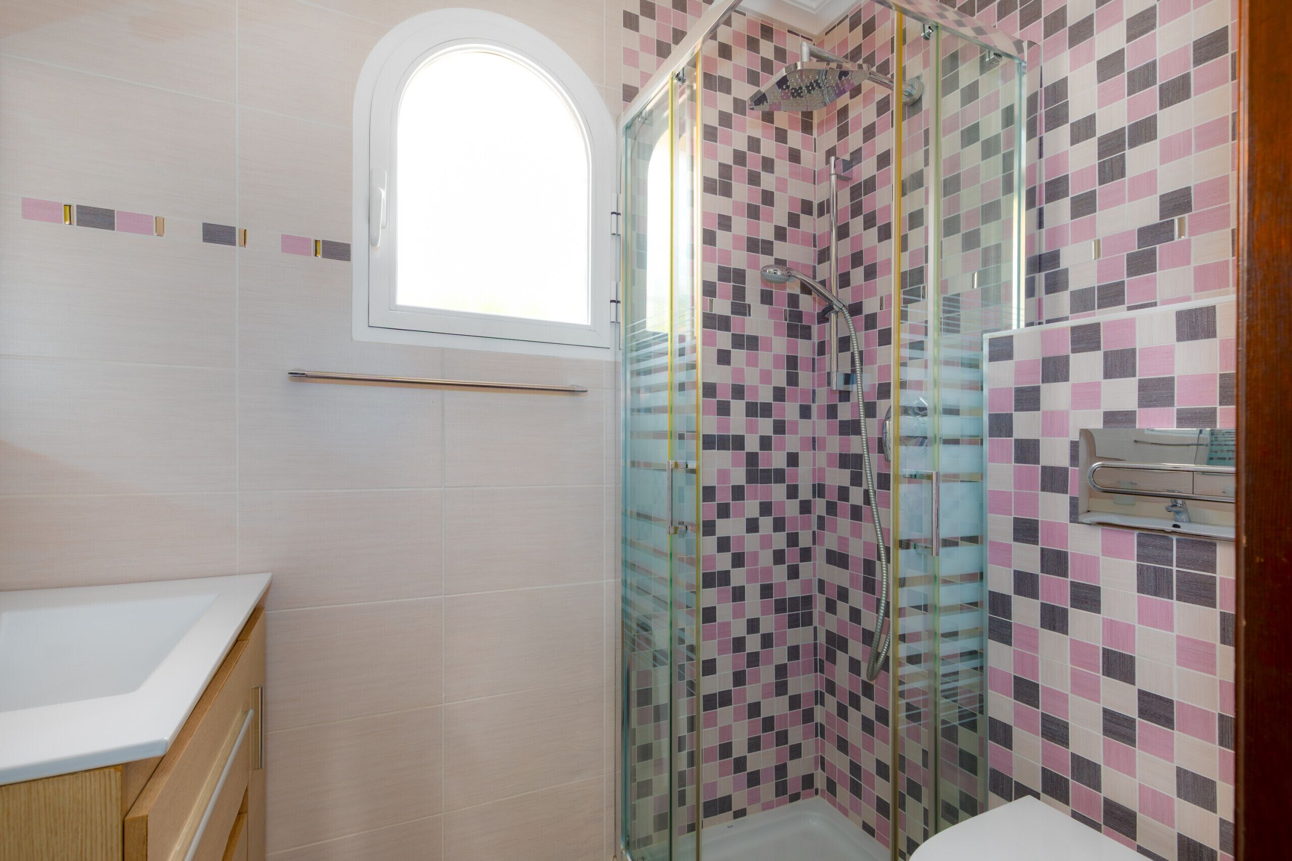 Une salle de bain avec une douche à parois de verre, un lavabo blanc et une fenêtre.