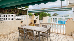 An outdoor patio with a stone floor, a wooden table with chairs, a barbecue grill, and a pool in the background. - Casa Nuestro Sueño for 4 People (Calpe / Calp)