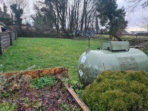 A green tank-like structure in a grassy area with a wooden bench and dense shrubbery.
