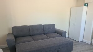 A grey sectional sofa in a room with a white wardrobe and a white door marked 'First Aid'. - Rural County Sligo Studio, Sleeps 2 With Parking (Ballintogher)