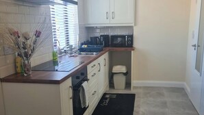 A compact kitchen with white cabinets, a microwave, a sink, and a trash bin. - Rural County Sligo Studio, Sleeps 2 With Parking (Ballintogher)