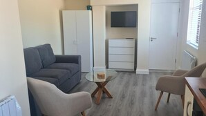 A compact living space with a grey sofa, two armchairs, a glass coffee table, a TV mounted on the wall, and a white cabinet. - Rural County Sligo Studio, Sleeps 2 With Parking (Ballintogher)