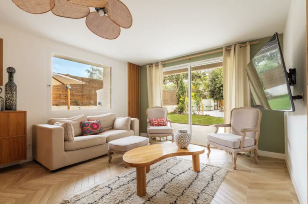A living room with a sofa, armchairs, a coffee table, and a TV mounted on the wall.