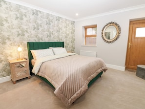 Un dormitorio con cama, mesita de noche, lámpara, espejo y puerta.