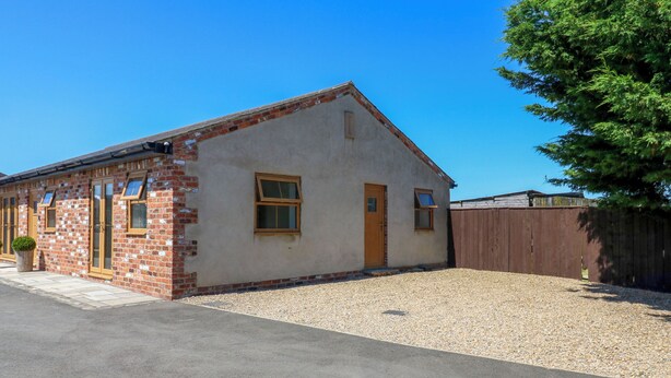 A single-story building with a brick facade, a gravel driveway, and a wooden fence. - Black Banks Farm Cottage (Darlington)