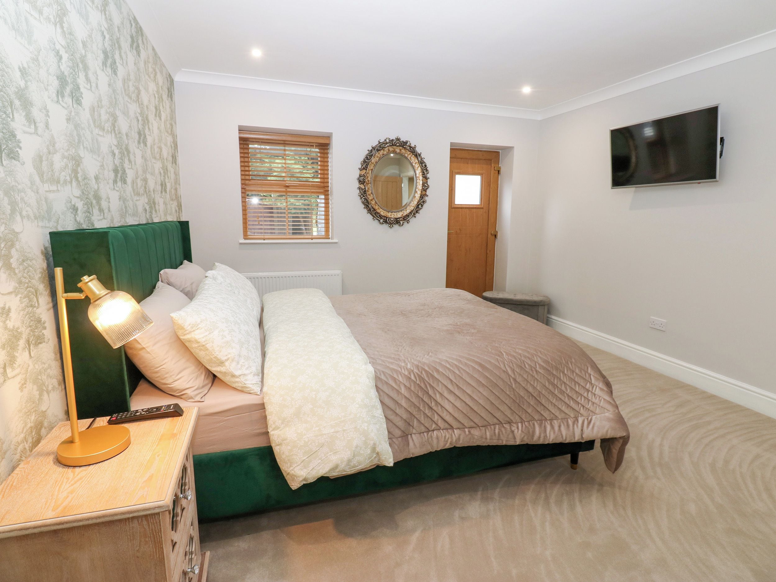 Un dormitorio con cama, mesita de noche, lámpara y televisor montado en la pared.