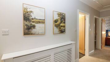 Um corredor com um radiador branco, duas pinturas de paisagens e uma porta que dá para outro quarto.