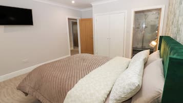 Un dormitorio con cama, televisor montado en la pared, armario y baño con puerta de cristal.