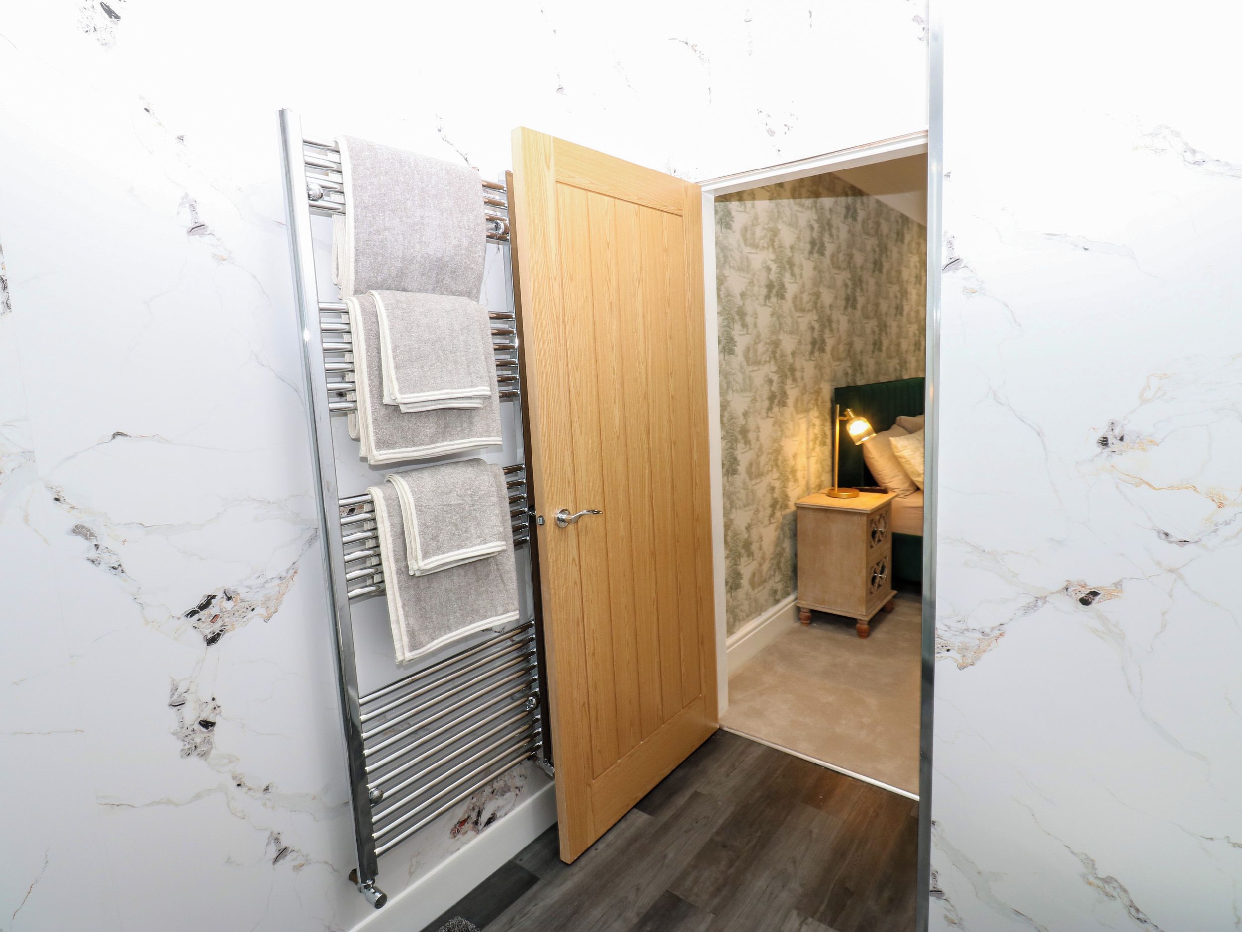 Un baño con puerta de madera, un perchero y una mesita de noche con lámpara.