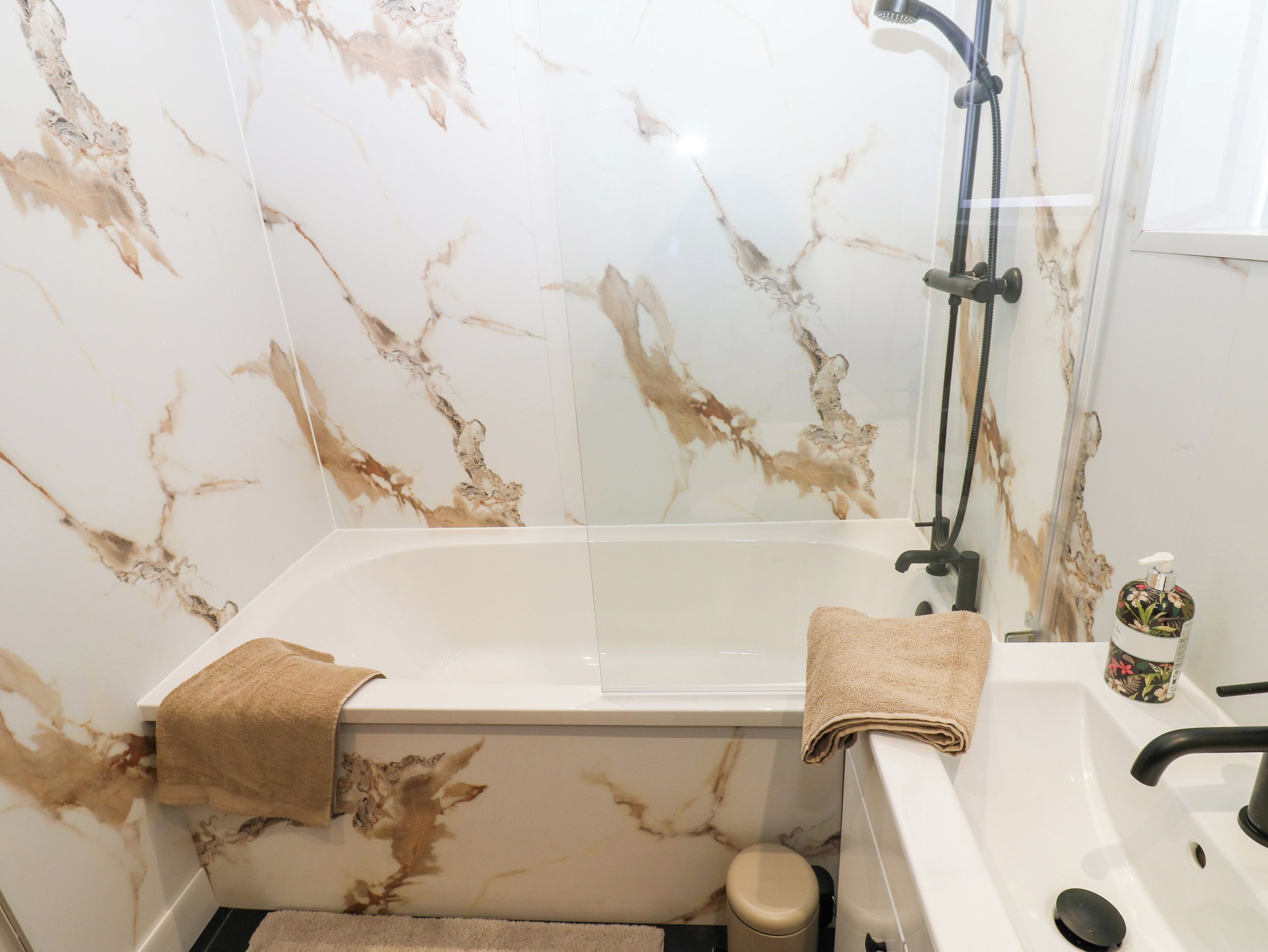 Ein Badezimmer mit Marmorwand, einer Badewanne, einer Dusche und einem Waschbecken mit Wasserhahn.