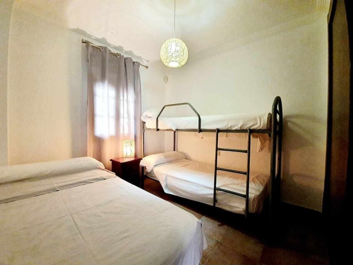A room with bunk beds, a bedside table with a lamp, and a window with curtains.