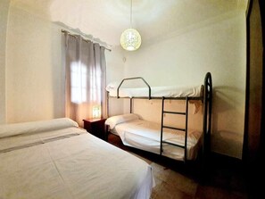 Ein Zimmer mit Etagenbetten, einem Nachttisch mit Lampe und einem fensterbepflanzten Fenster.
