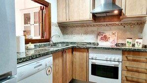 A compact kitchen with a dishwasher, oven, and wooden cabinets. - Los Pelícanos - Facing the sea, pool and garden - Ref.411F (Punta del Moral)