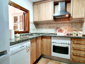 A compact kitchen with a dishwasher, oven, and wooden cabinets. - Los Pelícanos - Facing the sea, pool and garden - Ref.411F (Punta del Moral)