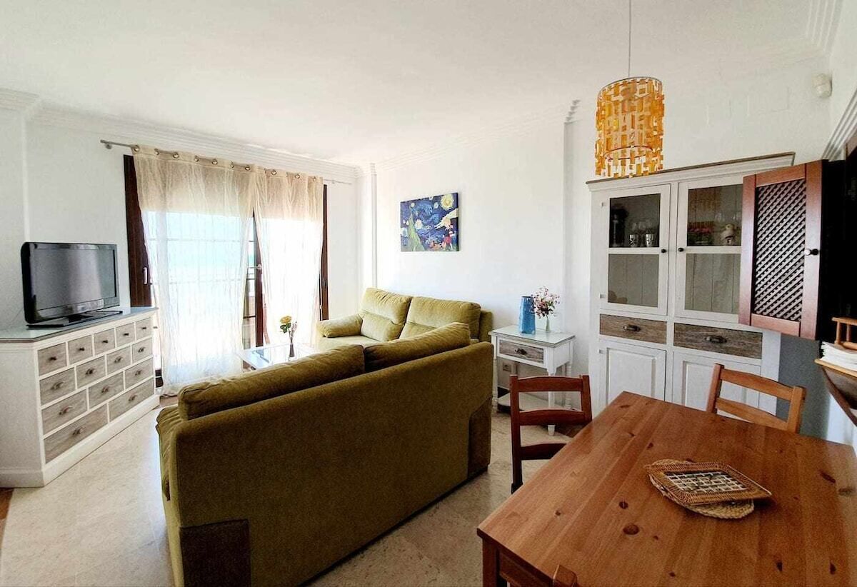 Een woonkamer met een bank, een televisie, een eettafel en een kast.