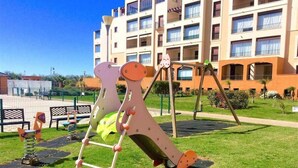 A playground with a slide and climbing structure in front of a building with multiple balconies. - Los Pelícanos - Facing the sea, pool and garden - Ref.411F (Punta del Moral)