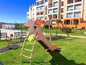 A playground with a slide and climbing structure in front of a building with multiple balconies. - Los Pelícanos - Facing the sea, pool and garden - Ref.411F (Punta del Moral)