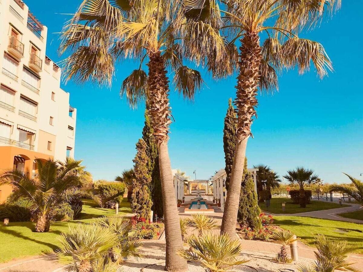 A hotel courtyard with palm trees, a fountain, and a building with balconies.