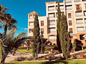 A multi-story hotel with a central courtyard, surrounded by palm trees and cypress trees. - Los Pelícanos - Facing the sea, pool and garden - Ref.411F (Punta del Moral)