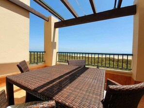 Ein Balkon mit Tisch und Stühlen, der auf einen Strand blickt.