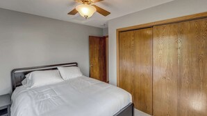 A bedroom with a bed, a wooden wardrobe, and a ceiling fan.