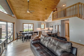 A spacious living room with a leather sofa, dining area, kitchen, and a staircase leading to an upper level.
