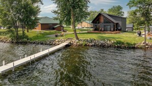 A lakeside cabin with a dock, a grassy area, and a building with a sloped roof.