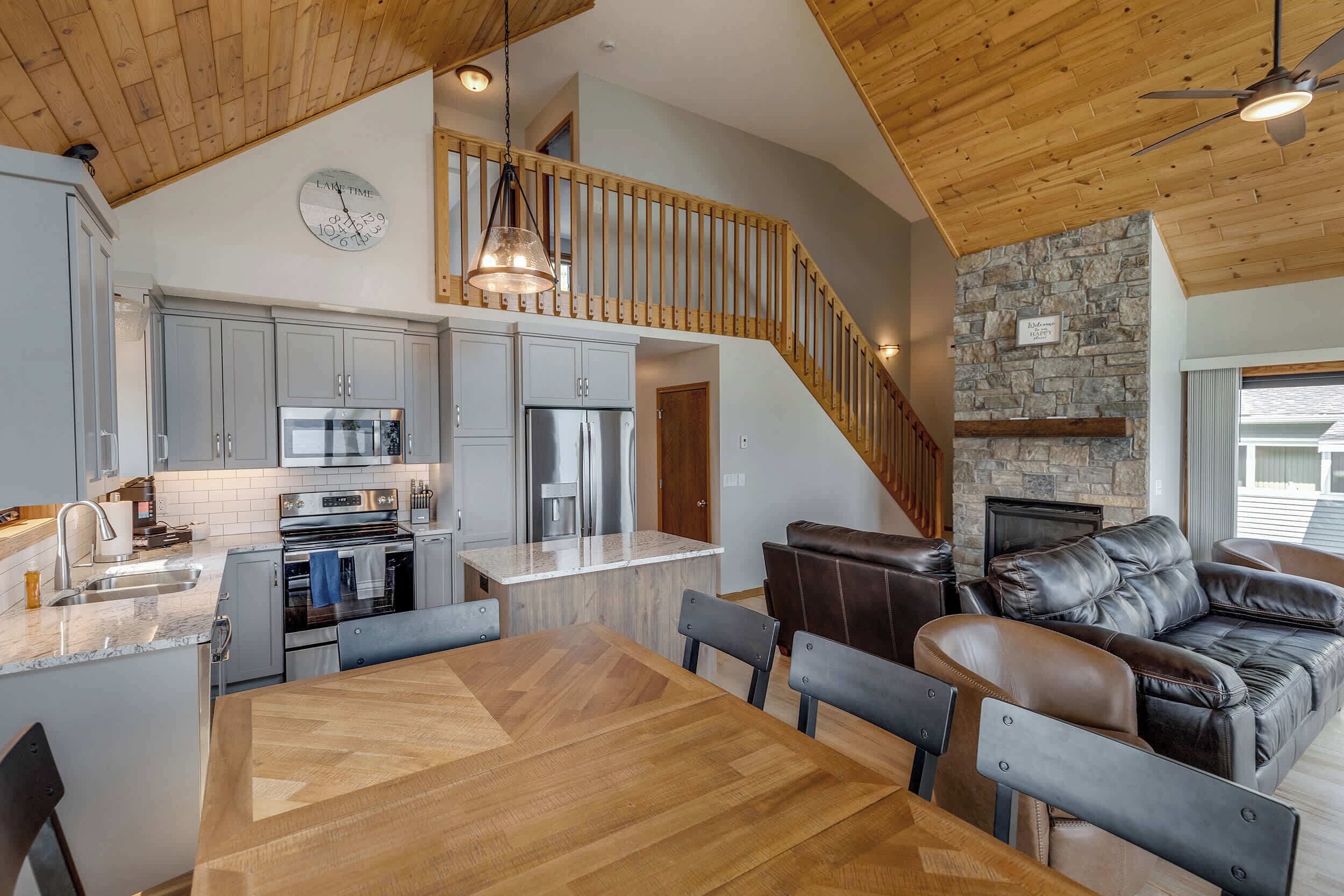 A modern kitchen with stainless steel appliances, a dining area with a wooden table and chairs, and a stone fireplace.