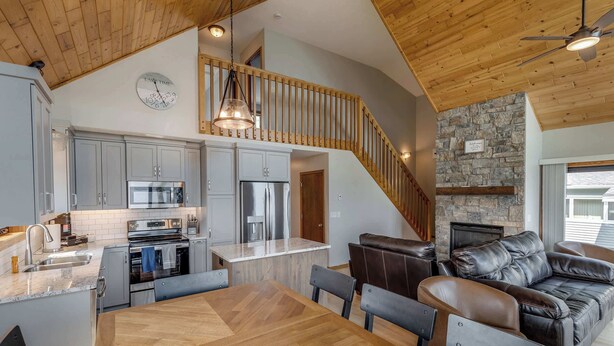 A modern kitchen with stainless steel appliances, a dining area with a wooden table and chairs, and a stone fireplace.