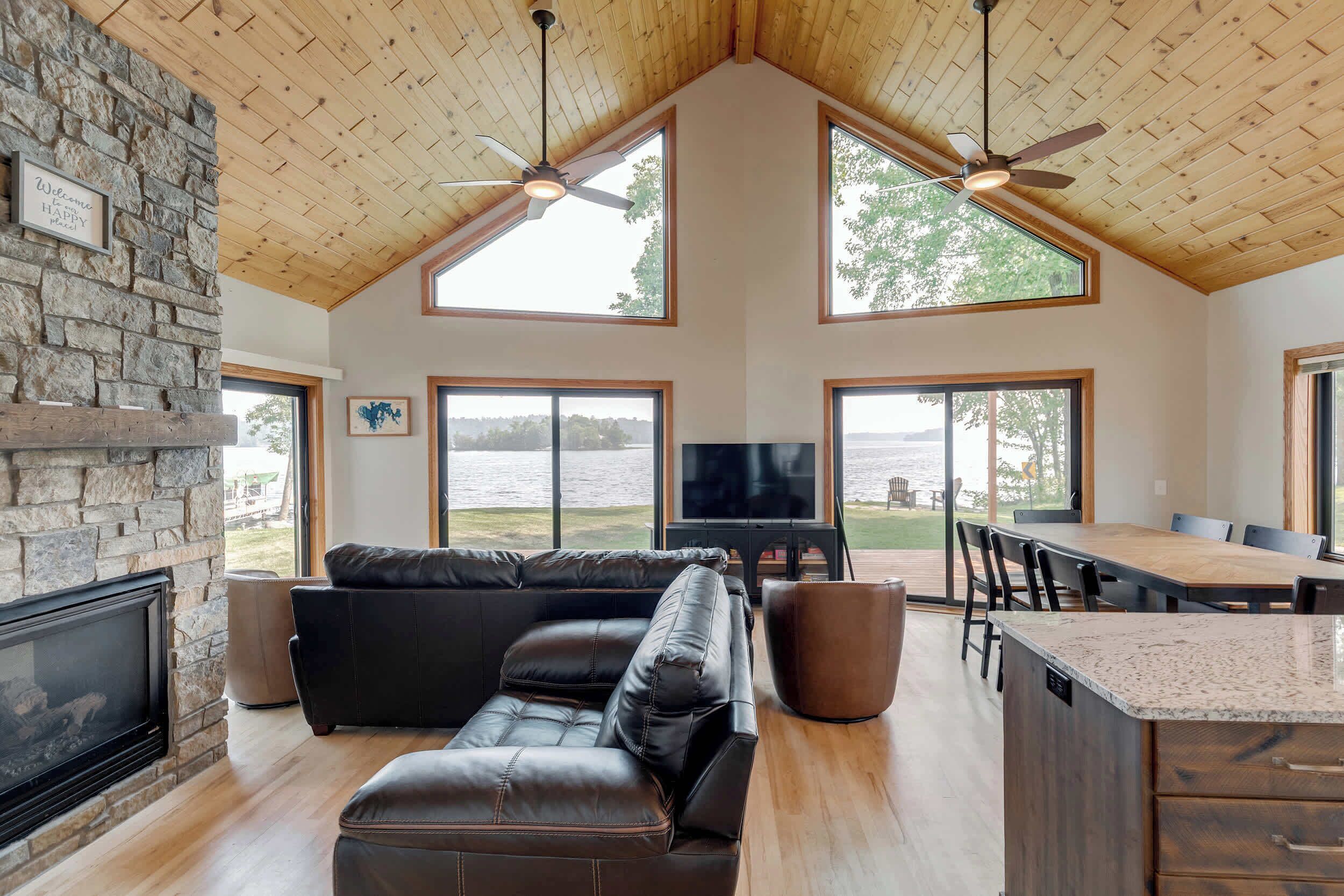 A spacious living area with a stone wall, a black leather sofa, a flat-screen TV, and a dining area with a wooden table and chairs.