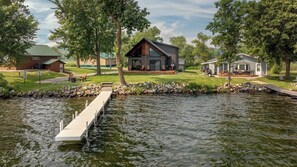 A lakeside property with a dock extending into the water, surrounded by well-maintained lawns and trees. - Great MEA and Fall Getaway Lakefront Cabin (Cushing)