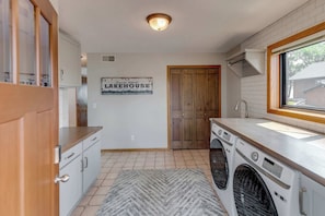 A kitchen with a wooden door, a sink, a washing machine, and a rug. - Great MEA and Fall Getaway Lakefront Cabin (Cushing)