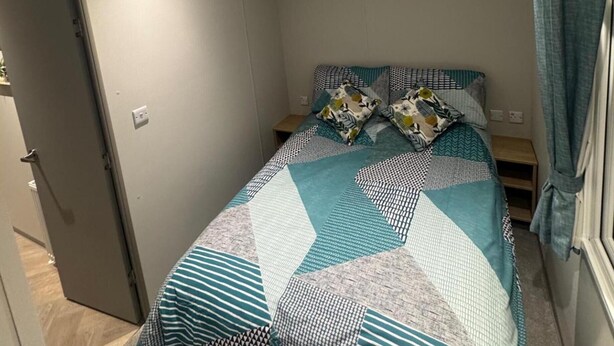 Un lit simple avec une couvre-lit à motifs et des oreillers, une table de chevet et une porte sur le côté gauche.