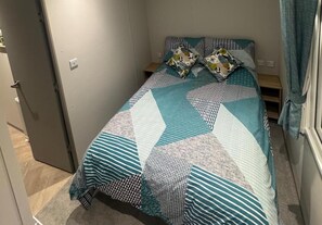 Una cama individual con una colcha y almohadas estampadas, una mesita de noche y una puerta a la izquierda.