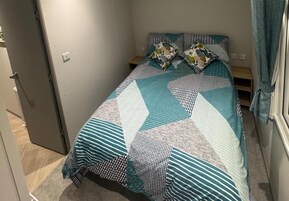 A single bed with a patterned bedspread and pillows, a bedside table, and a door to the left.