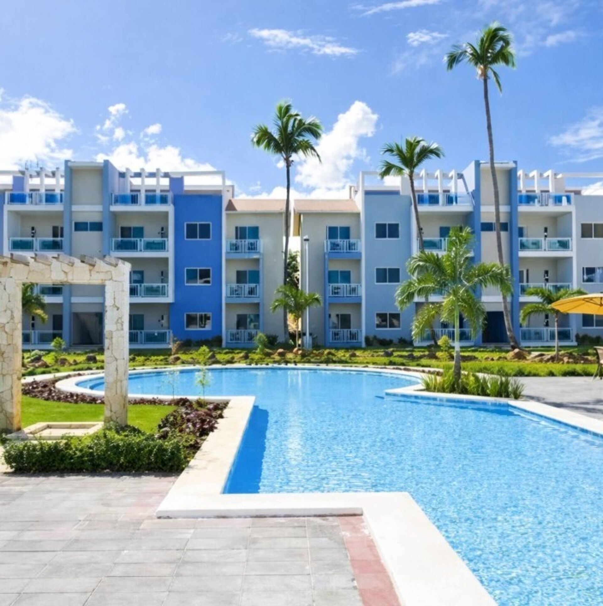 A resort with a swimming pool, palm trees, and multi-story buildings with balconies.