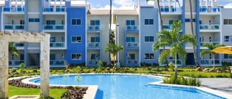 A resort with a swimming pool, palm trees, and multi-story buildings with balconies.